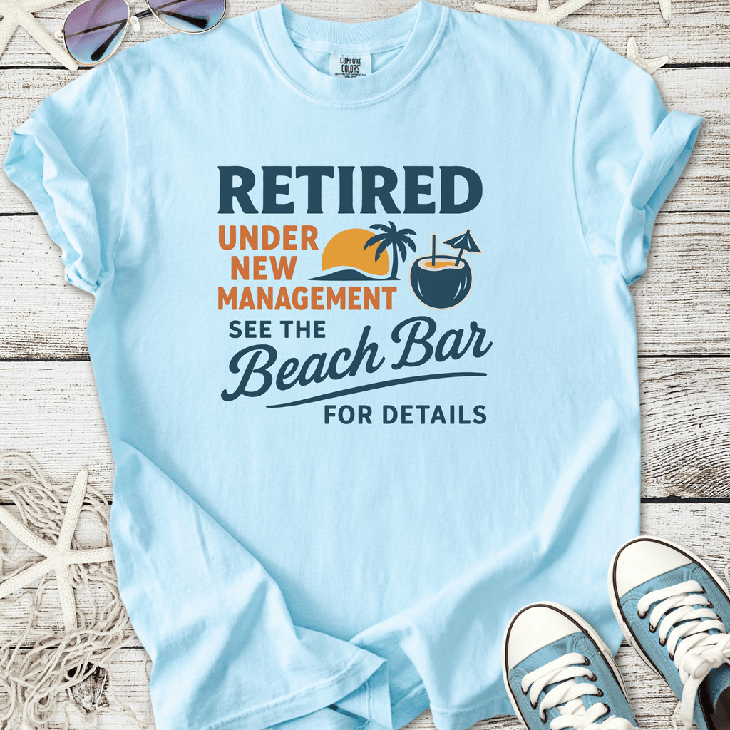 Light blue t-shirt with fun retirement graphic, featuring palm trees and beach bar theme.