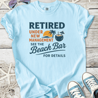 Light blue t-shirt with fun retirement graphic, featuring palm trees and beach bar theme.
