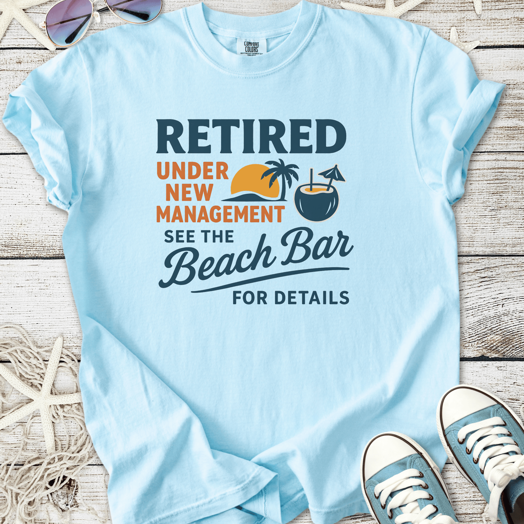 Light blue t-shirt with fun retirement graphic, featuring palm trees and beach bar theme.