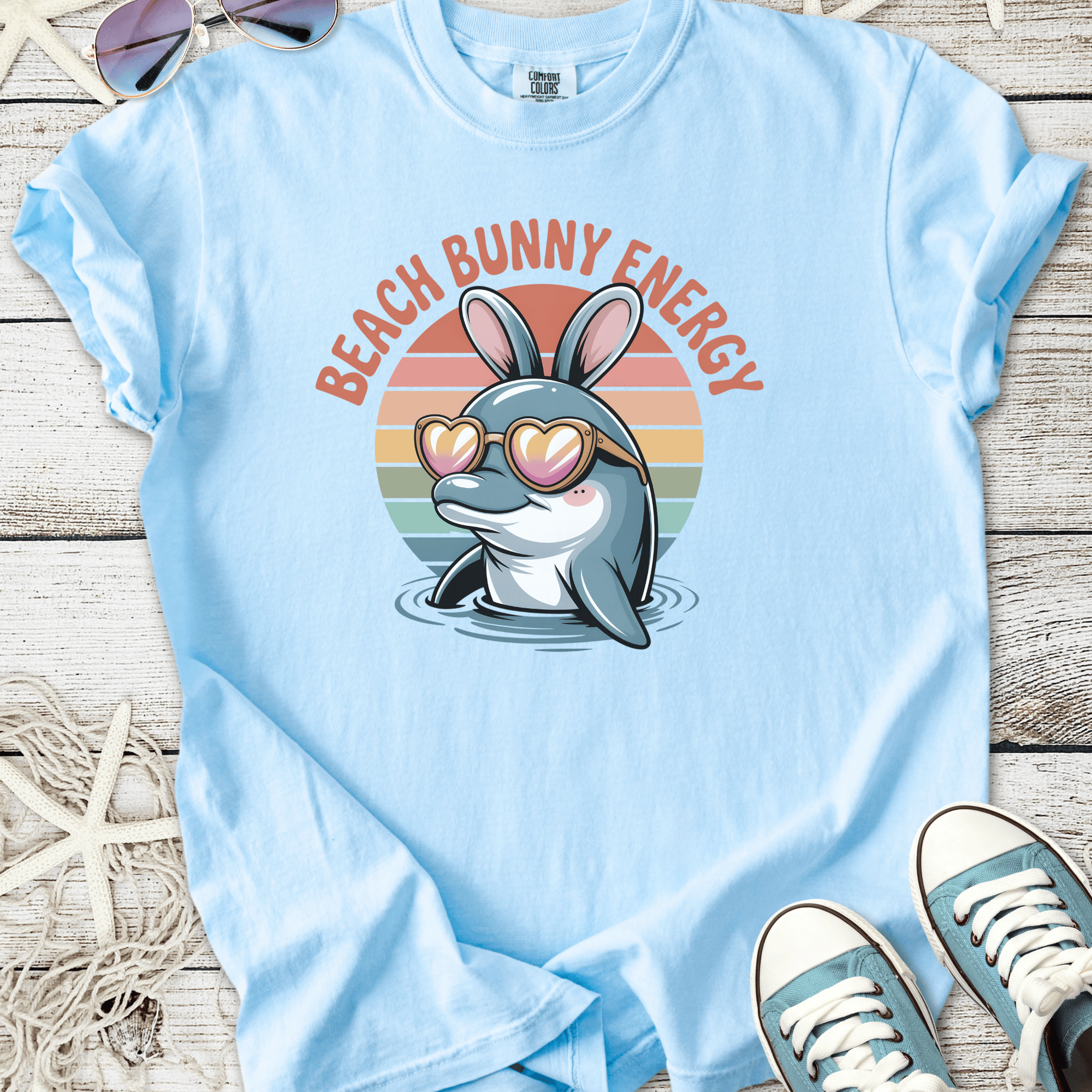 Light blue t-shirt featuring a playful dolphin graphic with bunny ears and heart sunglasses, perfect for summer.