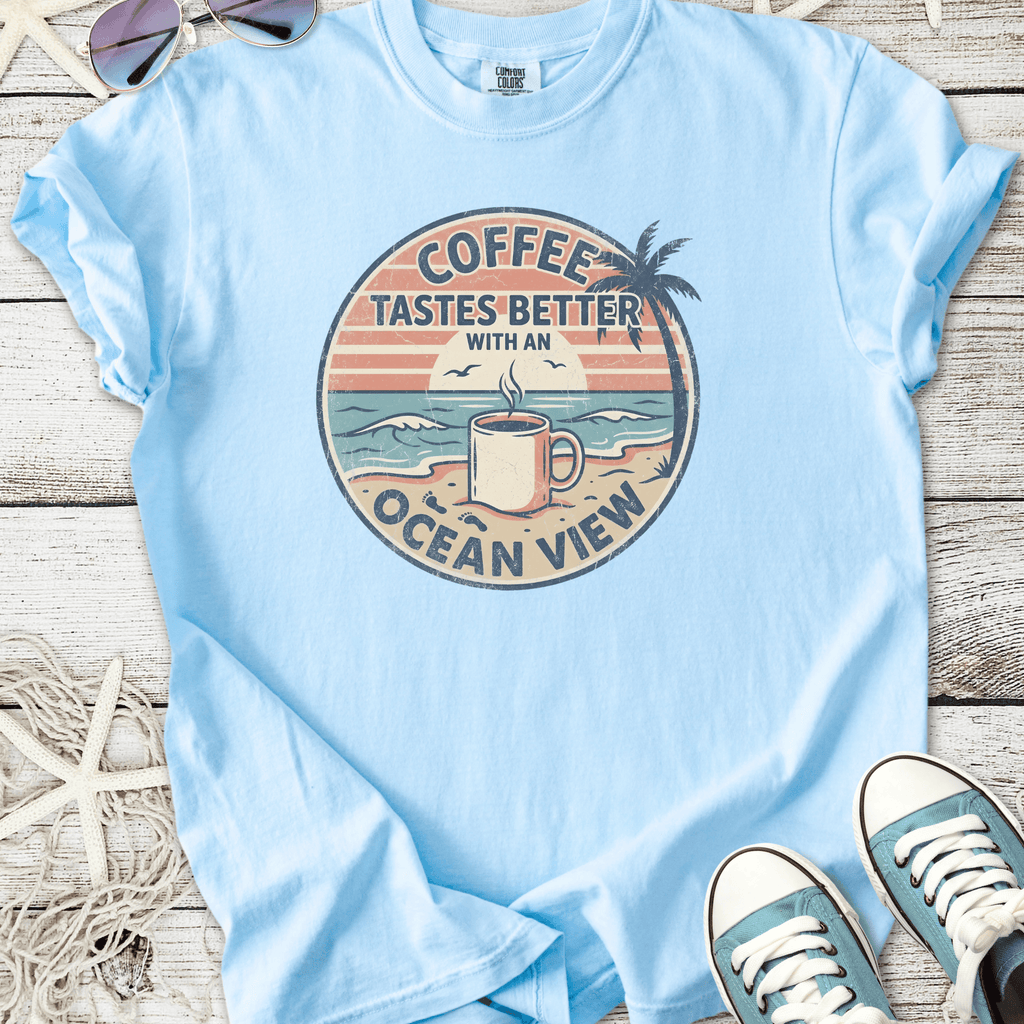 Light blue t-shirt featuring 'Coffee Tastes Better with an Ocean View' graphic, perfect for beach lovers.