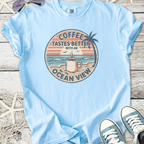 Light blue t-shirt featuring 'Coffee Tastes Better with an Ocean View' graphic, perfect for beach lovers.