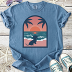 Blue graphic t-shirt featuring a dachshund by the beach at sunset with palm trees.