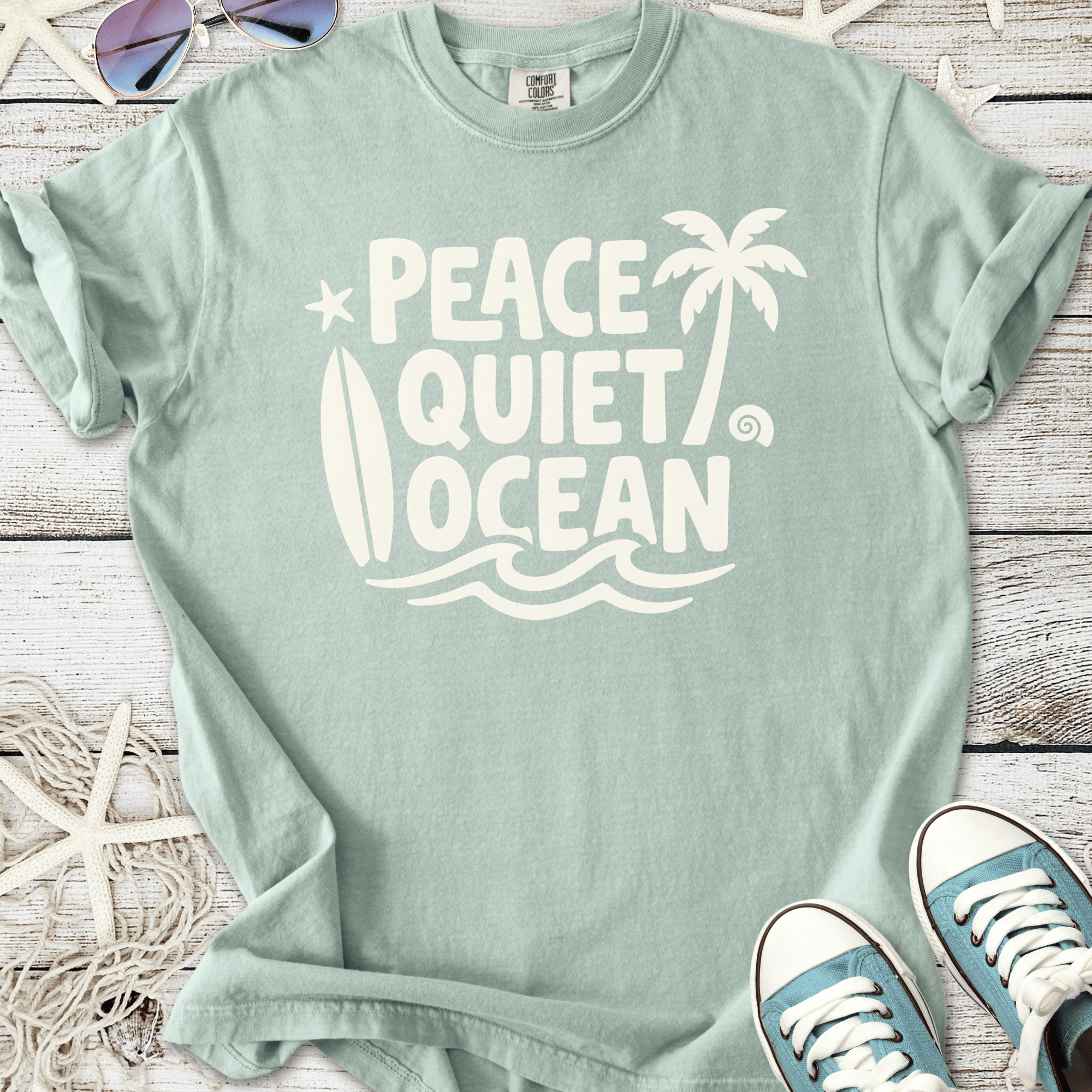 Mint green t-shirt featuring 'Peace Quiet Ocean' graphic, surfboard and palm trees, made of soft cotton.