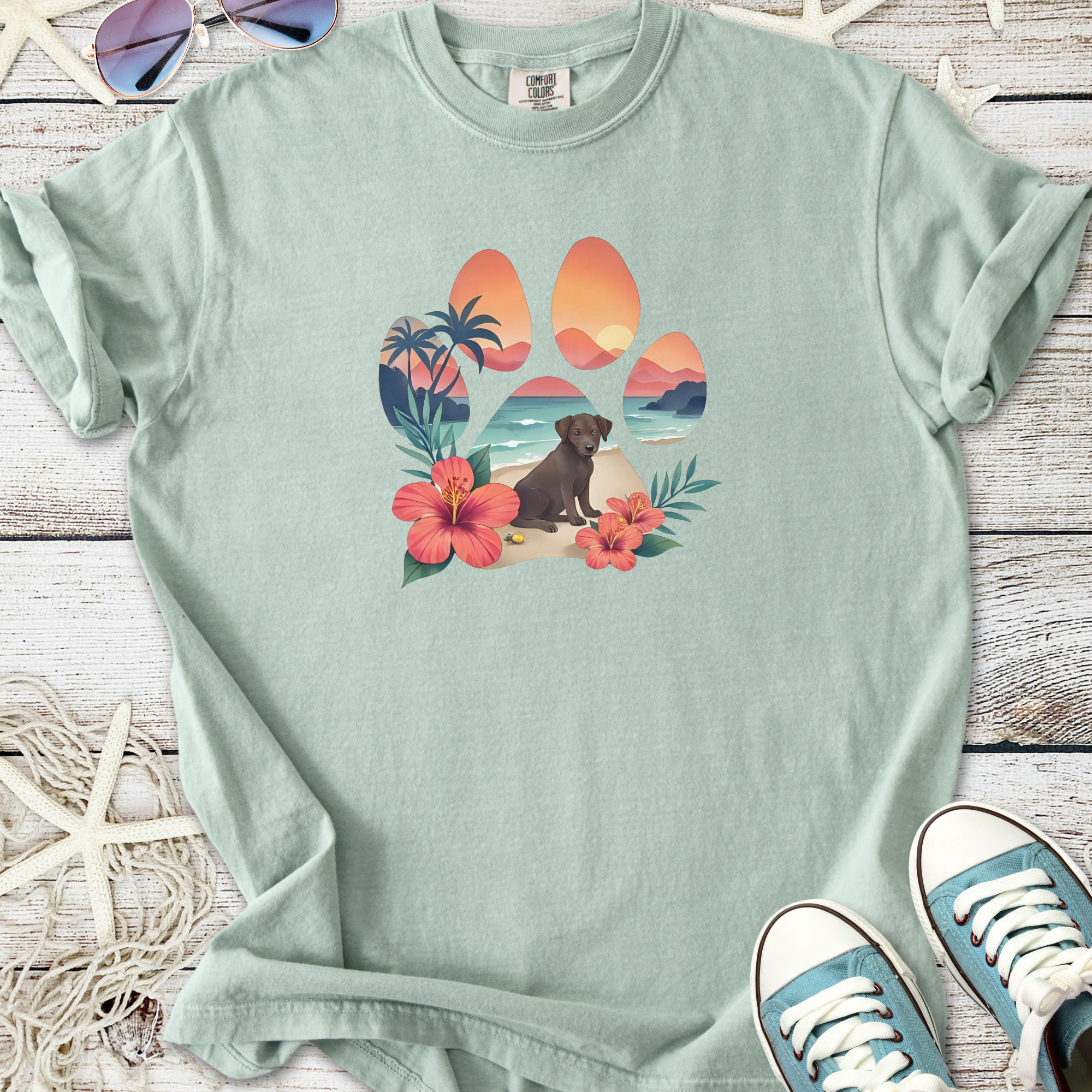 Light green t-shirt featuring a colorful dog paw design with beach and floral elements.