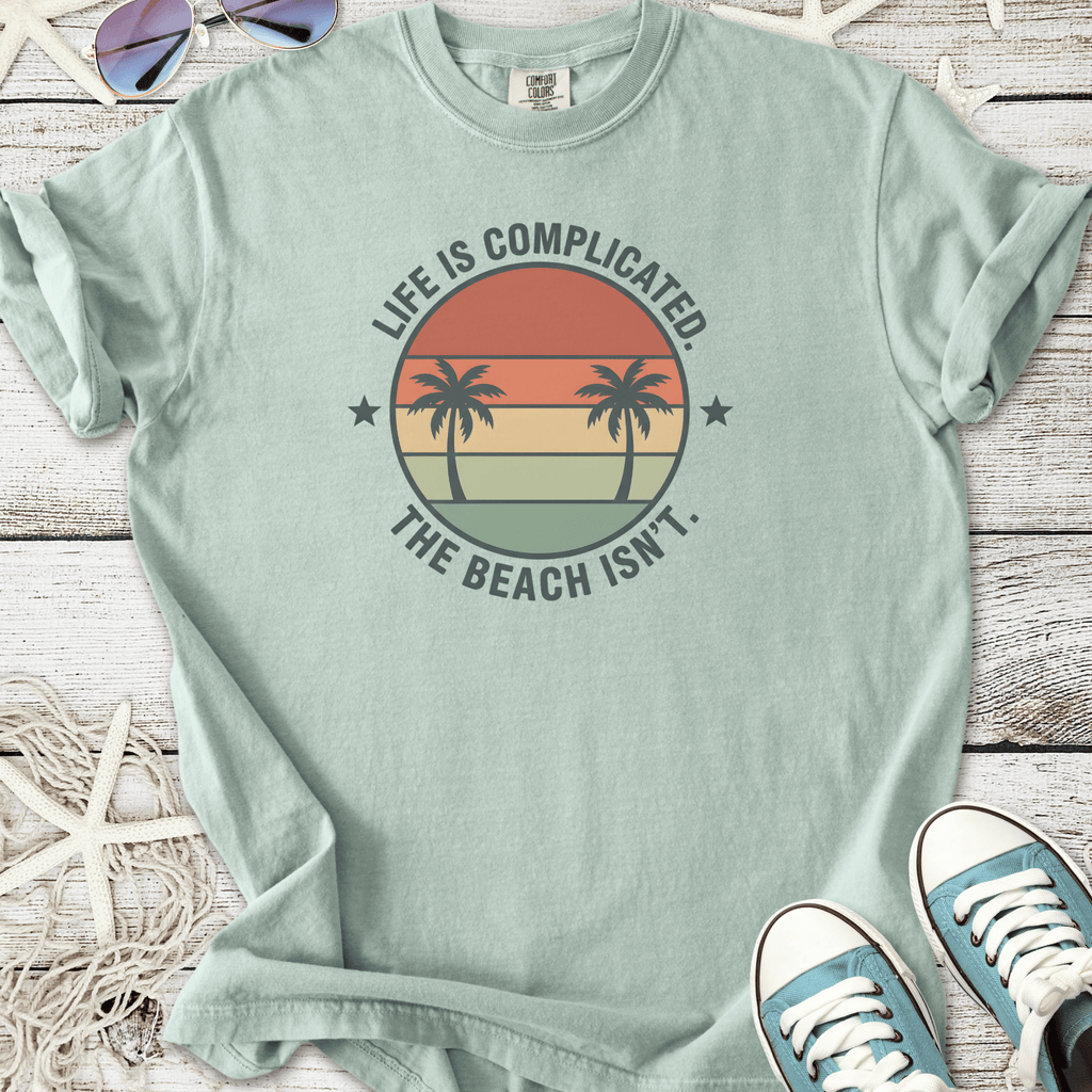 Light green t-shirt with palm tree graphic and 'Life is Complicated, The Beach Isn't' text.