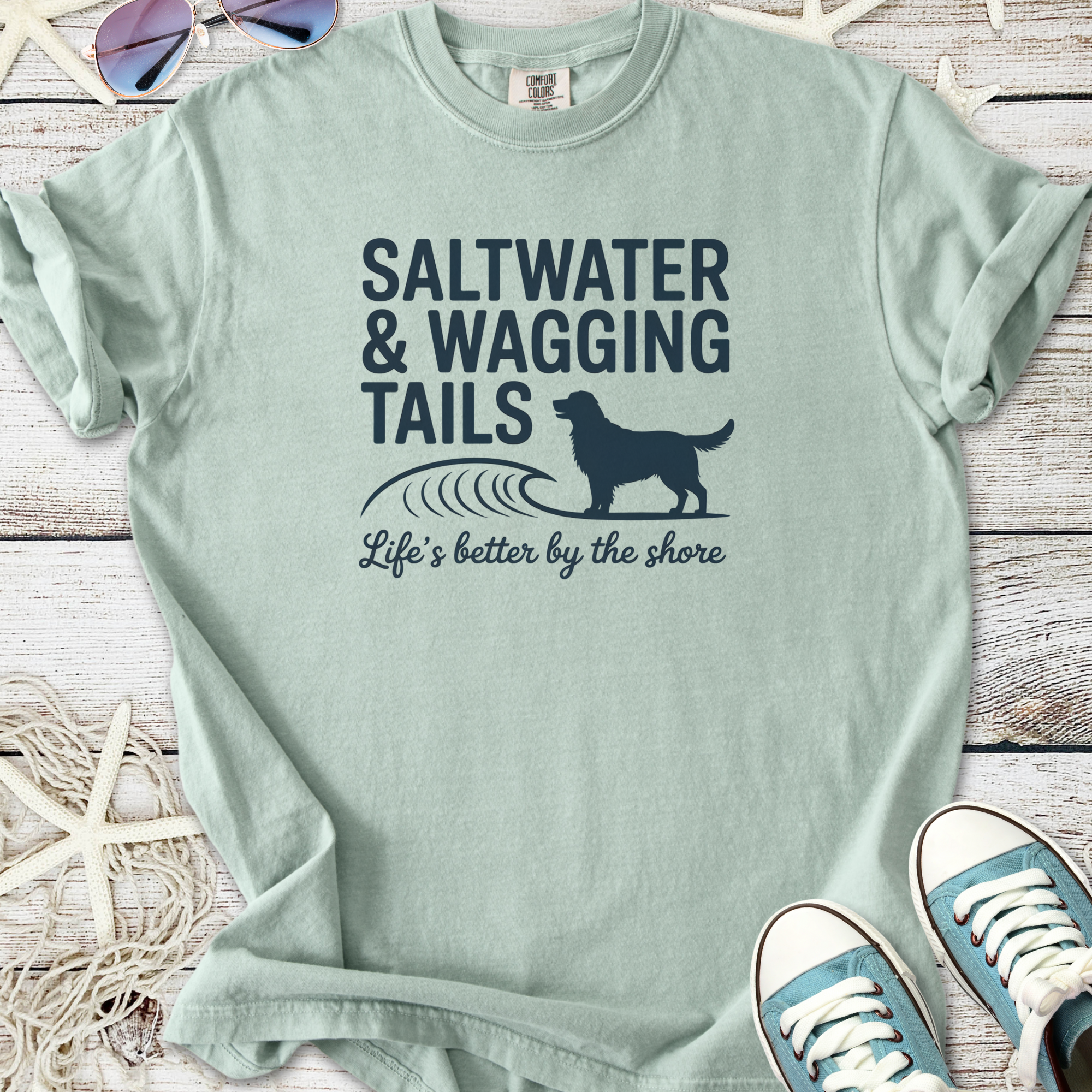 Light green t-shirt featuring 'Saltwater & Wagging Tails' graphic and dog design, perfect for beach lovers.