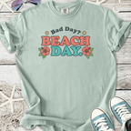 Light blue t-shirt with 'Bad Day? BEACH DAY.' graphic and floral design, perfect for casual beachwear.