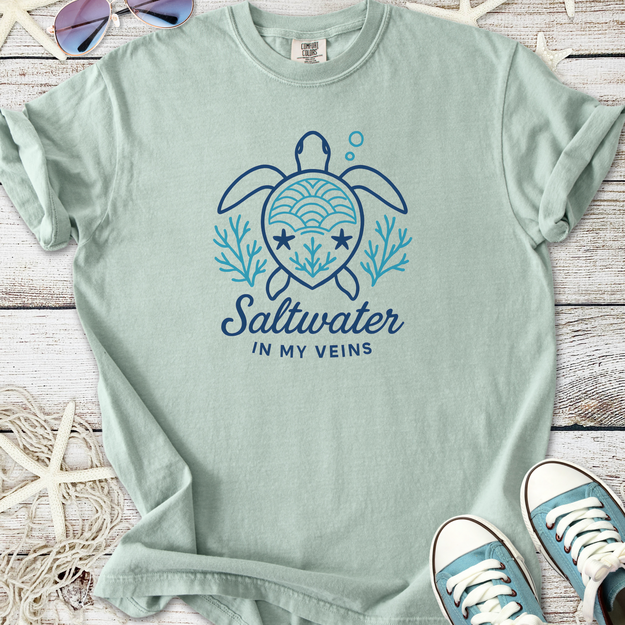 Light green t-shirt with turtle design and 'Saltwater in My Veins' text, perfect for beach lovers.
