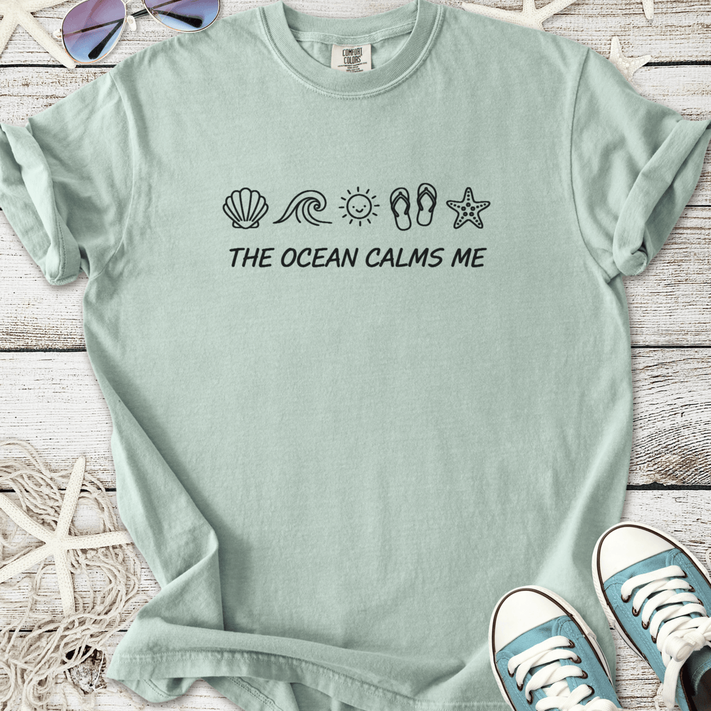 Light teal t-shirt with 'The Ocean Calms Me' print and beach-themed graphics. Comfortable cotton material.