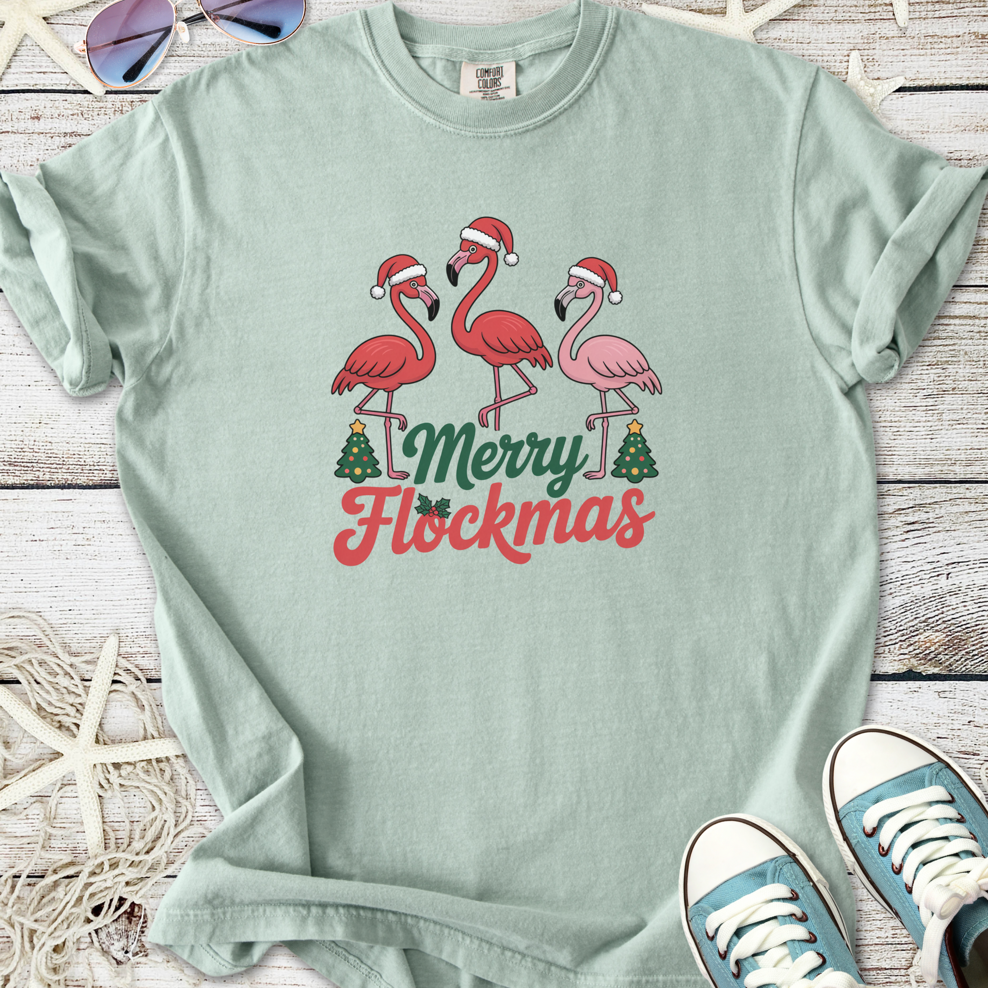 Mint green t-shirt featuring 'Merry Flockmas' and festive flamingos with Santa hats.