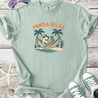 Light blue t-shirt with 'Paws & Relax' graphic, featuring a dog lounging in a hammock, tropical theme.