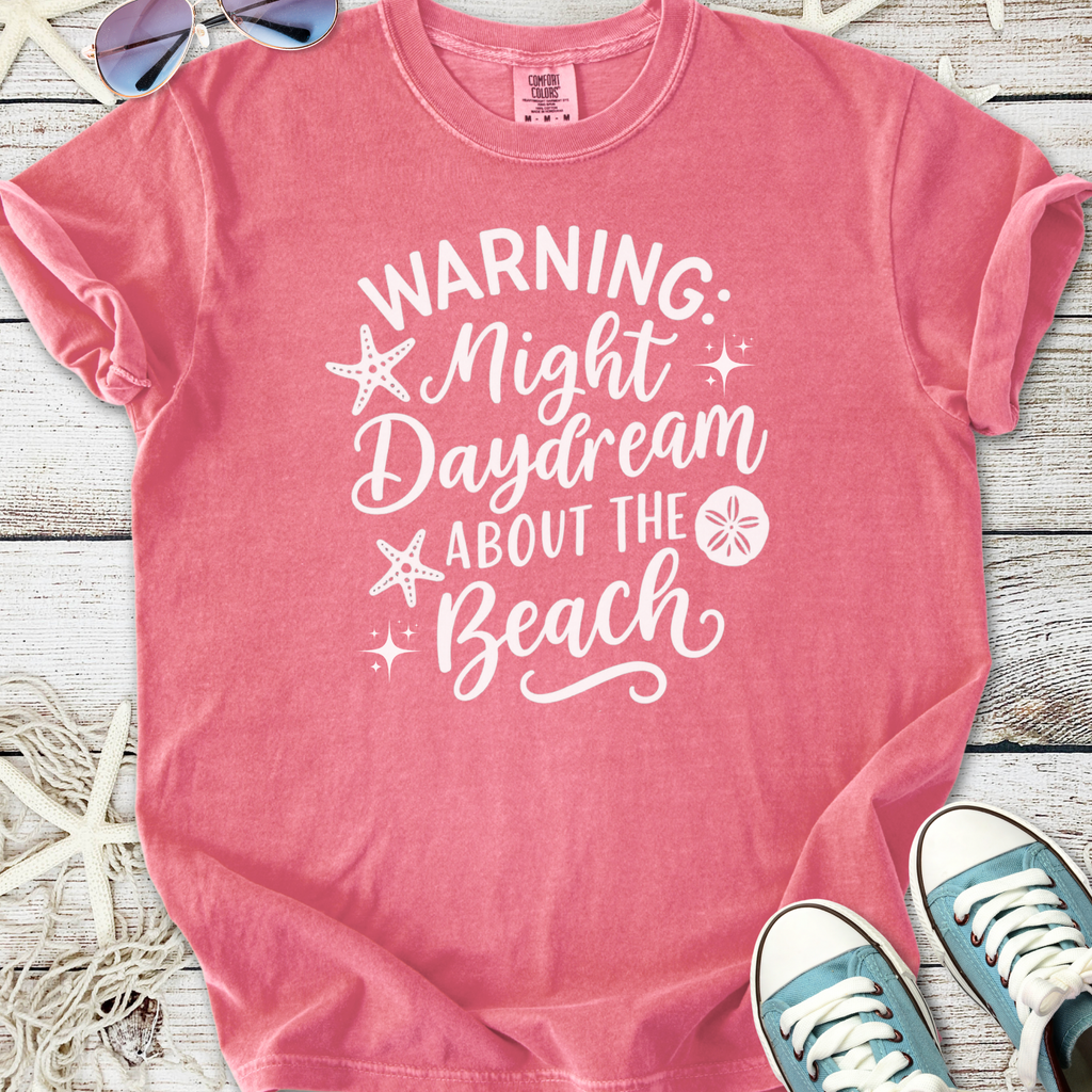 Pink graphic t-shirt with 'Warning: Night Daydream About the Beach' print, perfect for beach lovers.