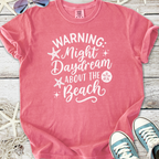 Pink graphic t-shirt with 'Warning: Night Daydream About the Beach' print, perfect for beach lovers.
