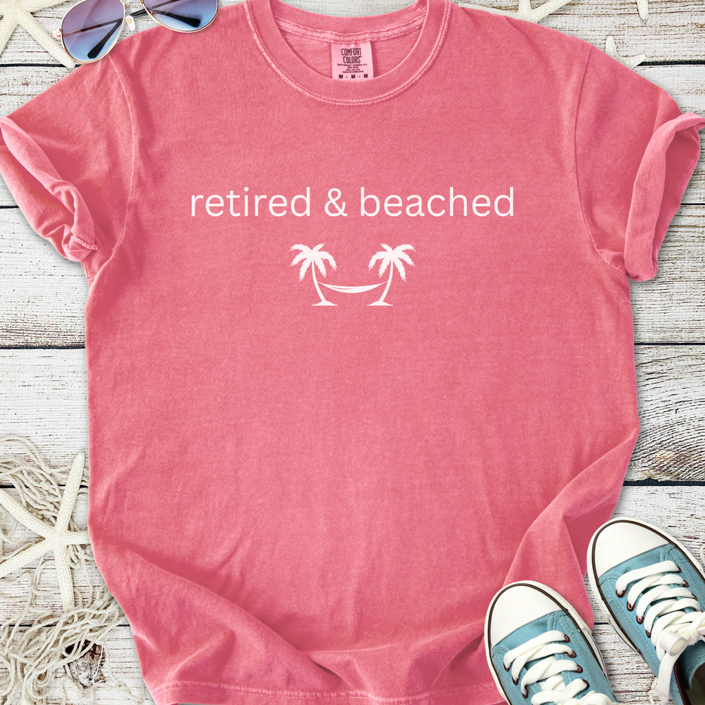 Pink cotton t-shirt with 'retired & beached' text and palm tree design, perfect for casual beachwear.