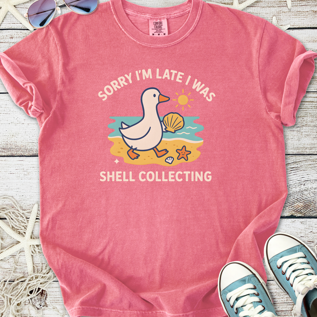 Pink graphic tee with duck design and 'Sorry I'm Late I Was Shell Collecting' slogan, perfect for beach lovers.