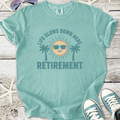 Light teal retirement t-shirt with a sun and palm trees graphic, perfect for vacation vibes.
