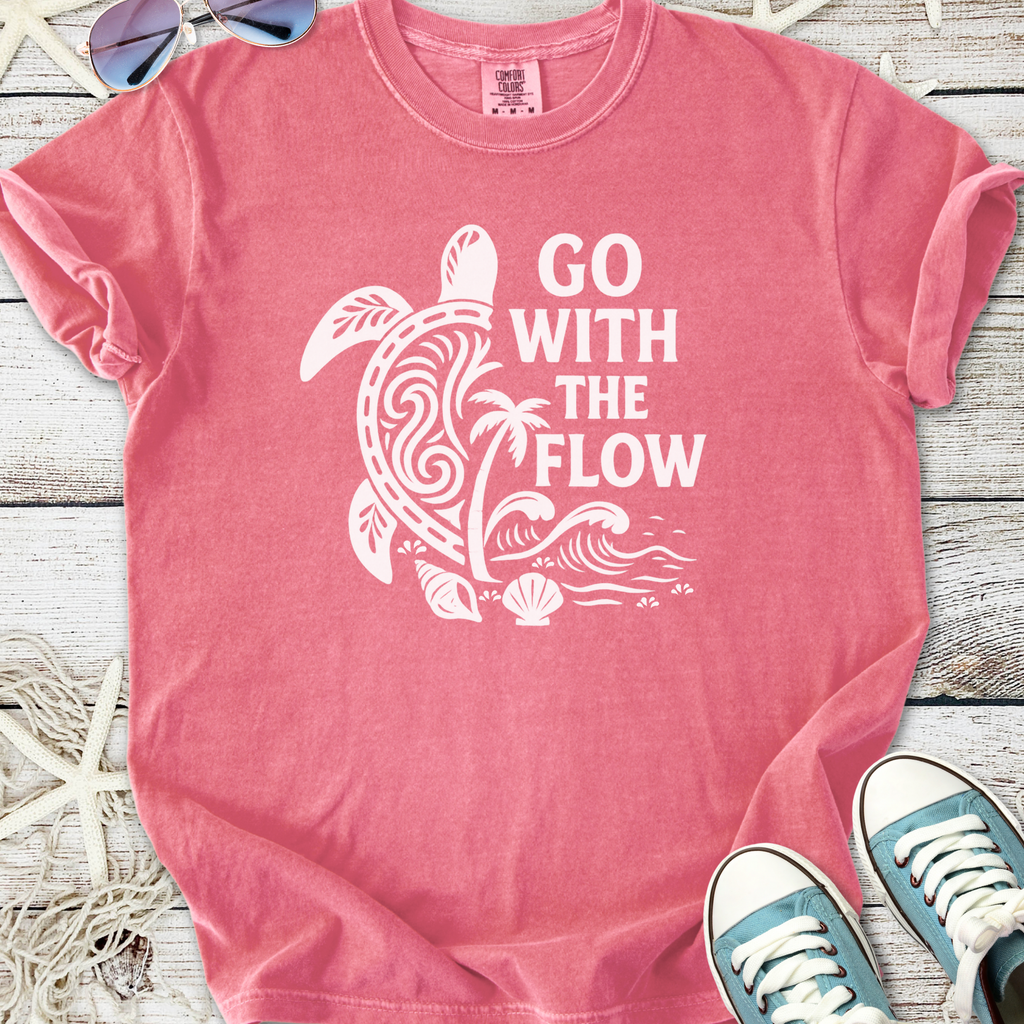 Pink graphic tee with 'Go With The Flow' design featuring turtle, palm tree, and ocean waves.
