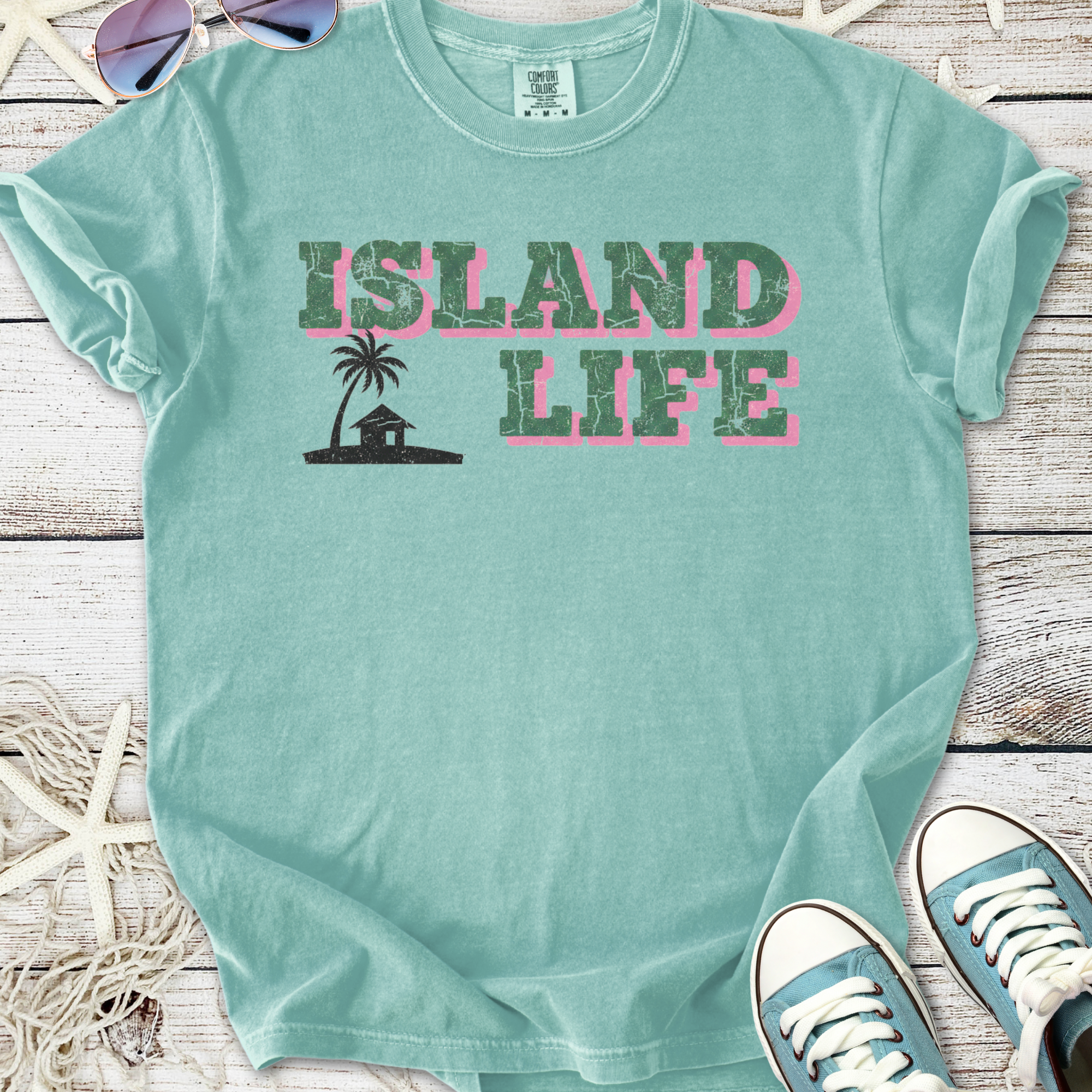 Light blue t-shirt with 'Island Life' graphic, featuring palm tree and house design, 100% cotton.