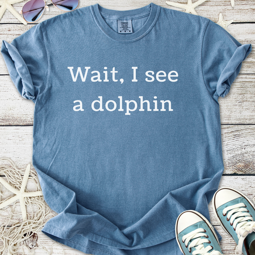 Light blue t-shirt with the text 'Wait, I see a dolphin' in white, made from soft and comfortable cotton.