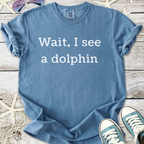 Light blue t-shirt with the text 'Wait, I see a dolphin' in white, made from soft and comfortable cotton.