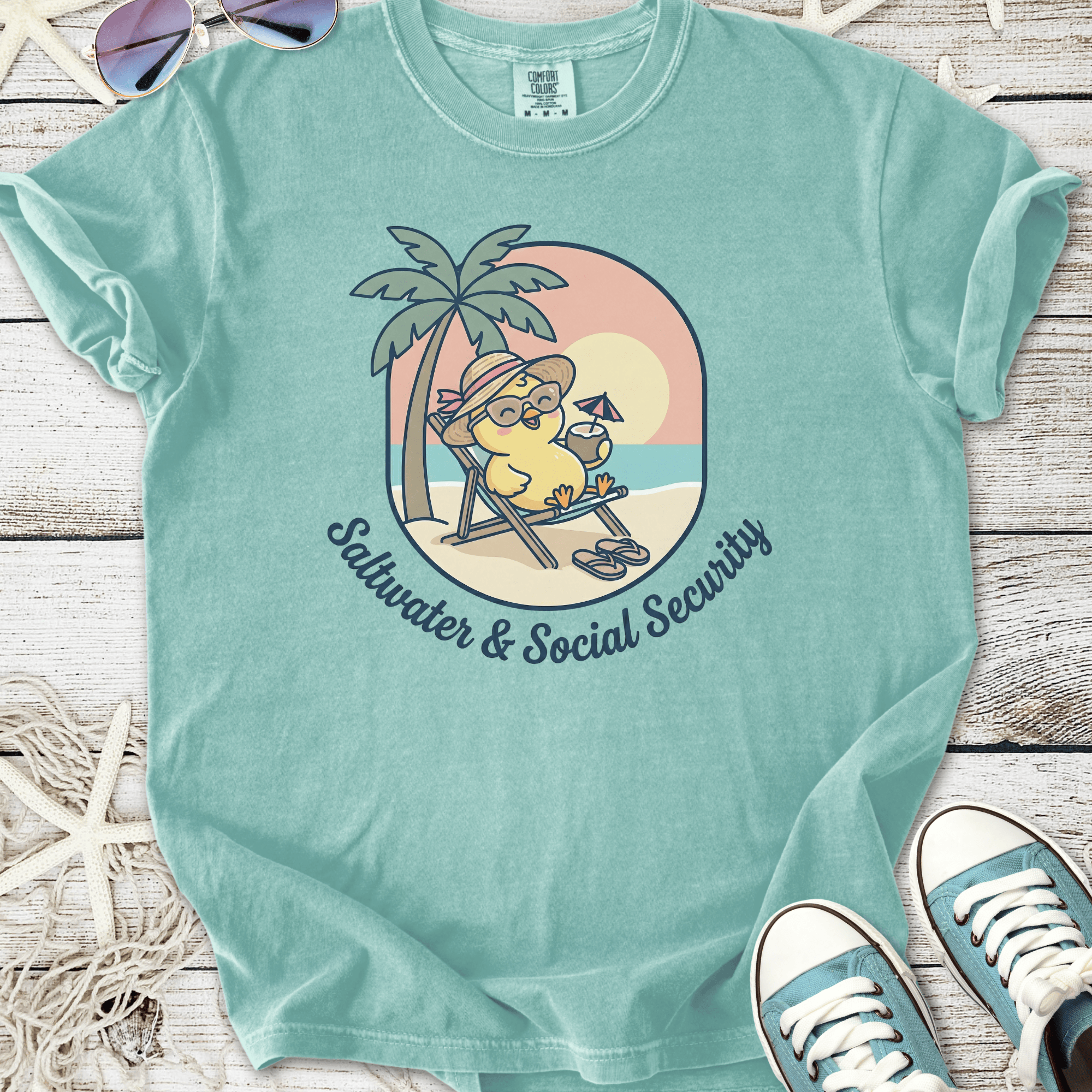 Turquoise cotton t-shirt featuring a cartoon character relaxing under palm trees with the text 'Saltwater & Social Security'.
