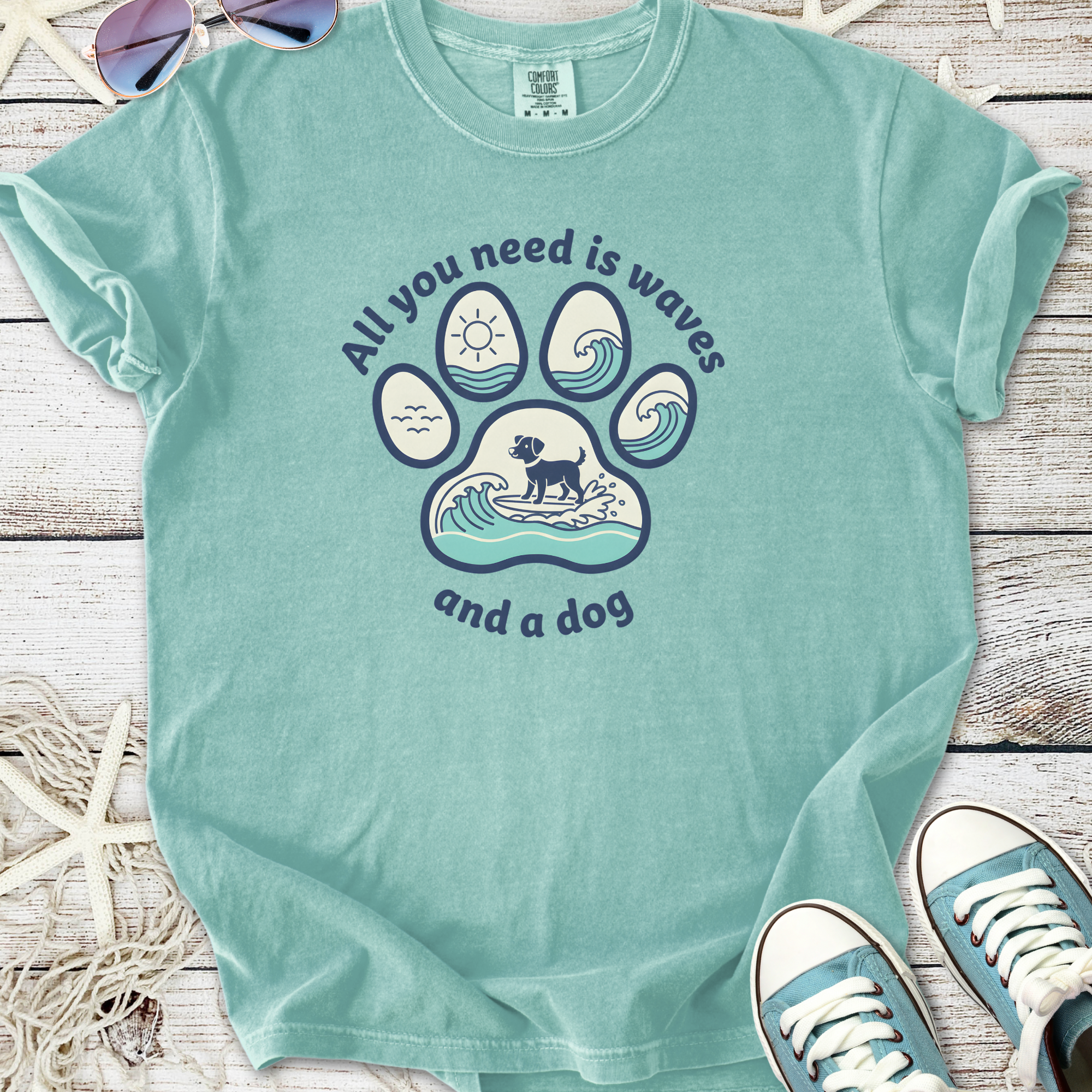 Light teal t-shirt featuring a dog paw print design with waves, text: 'All you need is waves and a dog'.