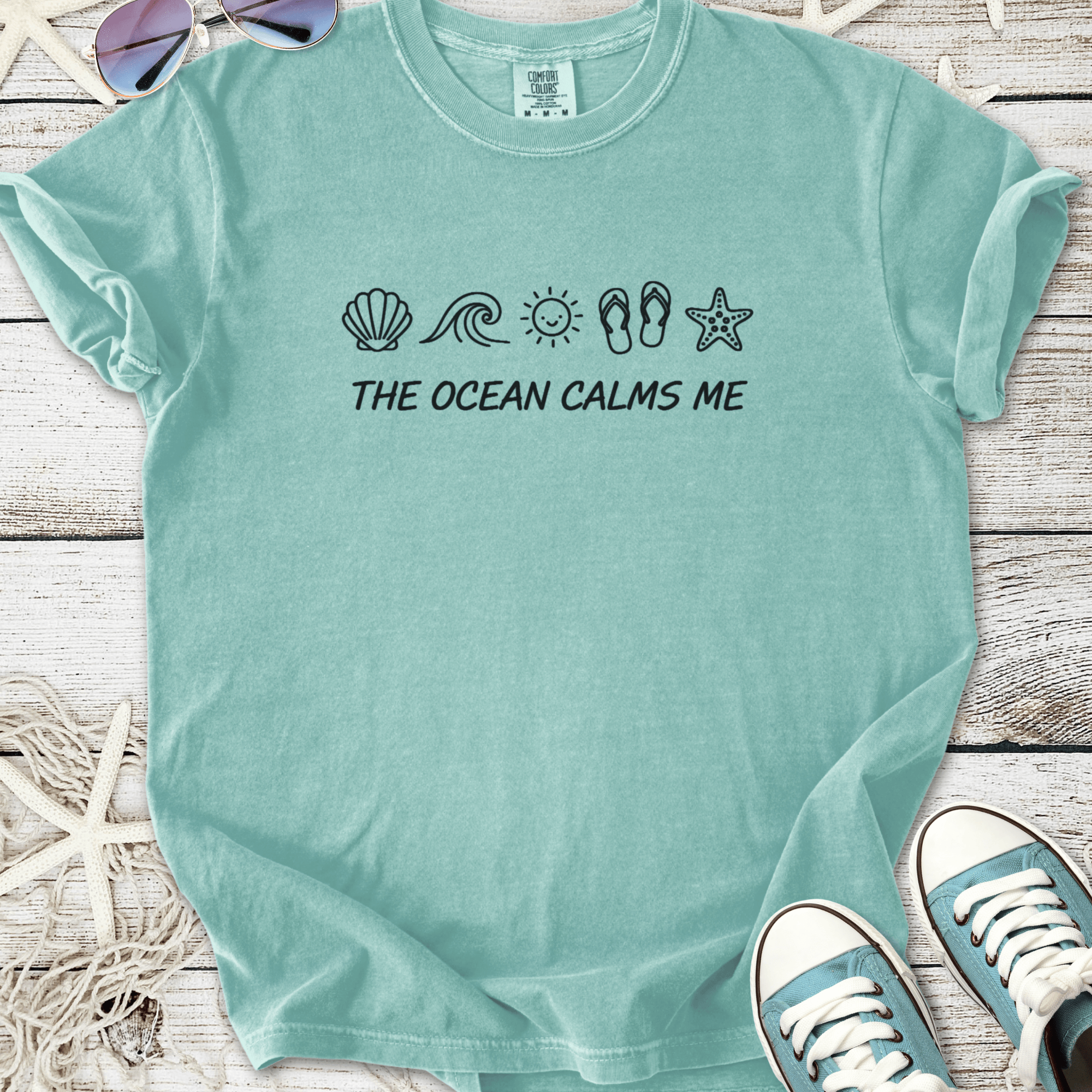 Light blue t-shirt with 'THE OCEAN CALMS ME' graphic and beach-themed icons, soft cotton material.