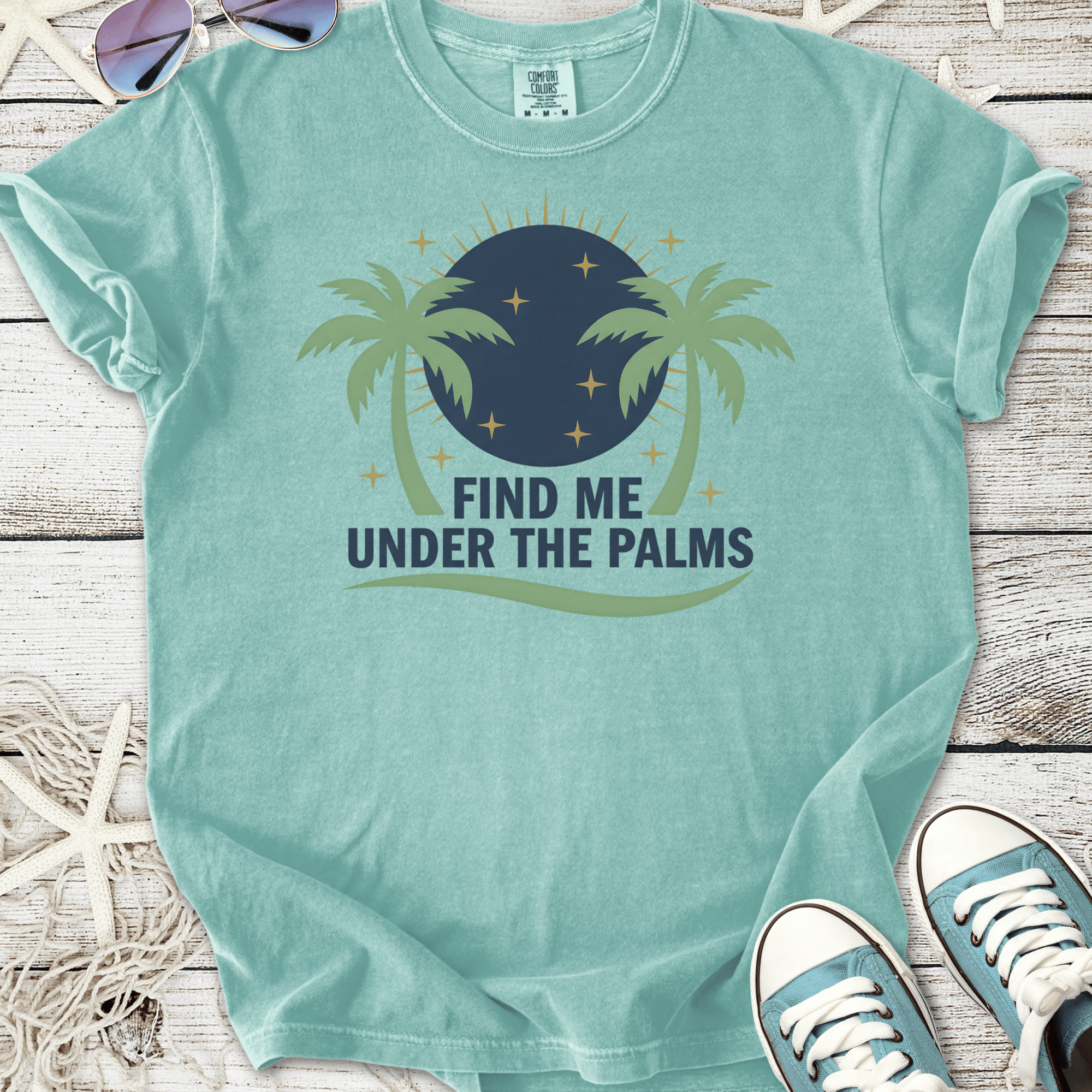 Light teal graphic tee featuring 'Find Me Under The Palms' with palm tree design and round moon.