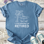 Blue cotton t-shirt with 'I Love Waking Up Retired' graphic, featuring palm trees and beach chairs.