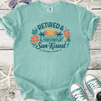 Mint green t-shirt featuring 'Retired & Sun-Kissed' design with flowers and sunset, ideal for island living.