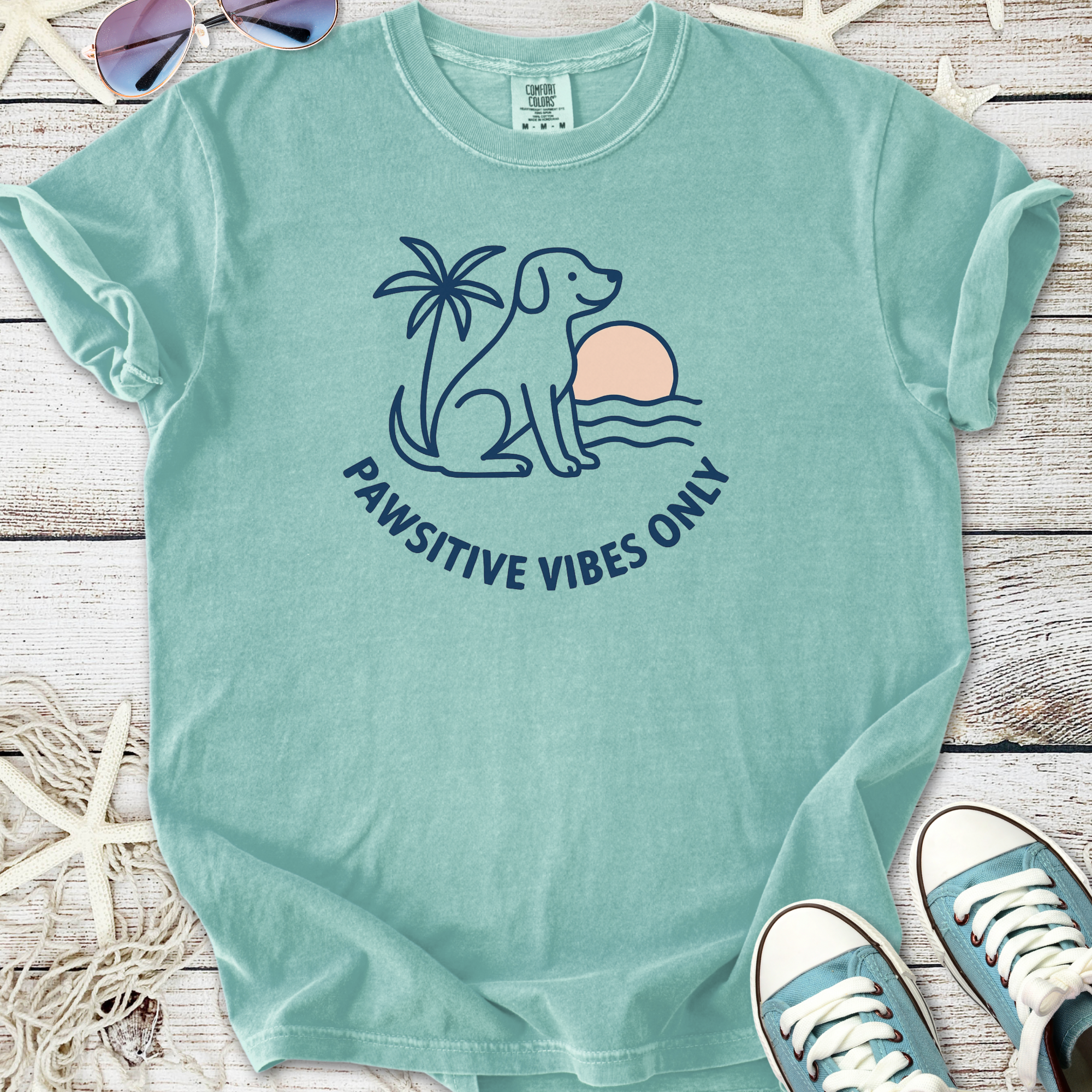 Mint green t-shirt featuring a dog, palm tree, and sunset with 'Pawsitive Vibes Only' slogan.