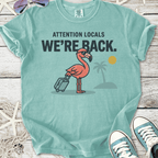 Light blue t-shirt featuring a pink flamingo with suitcase, text 'We're Back.' for summer vibes.