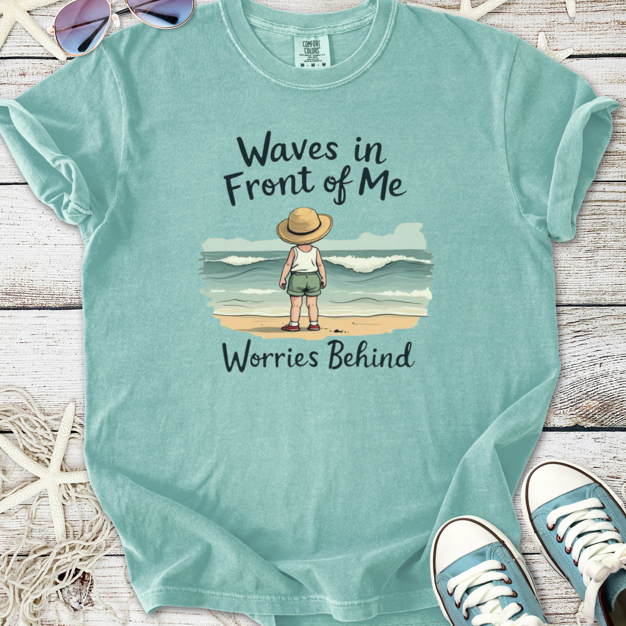 Mint green t-shirt featuring a child looking at waves with 'Waves in Front of Me, Worries Behind' text.