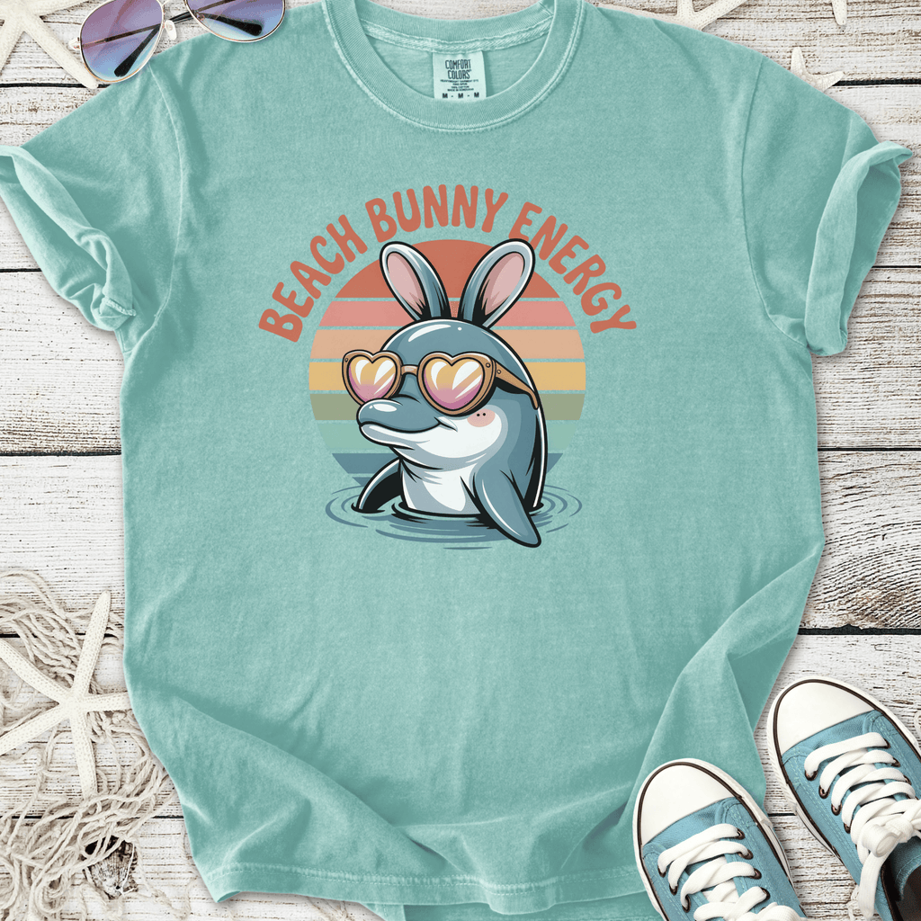 Light teal t-shirt featuring a cartoon dolphin with bunny ears and heart sunglasses, labeled 'Beach Bunny Energy'.