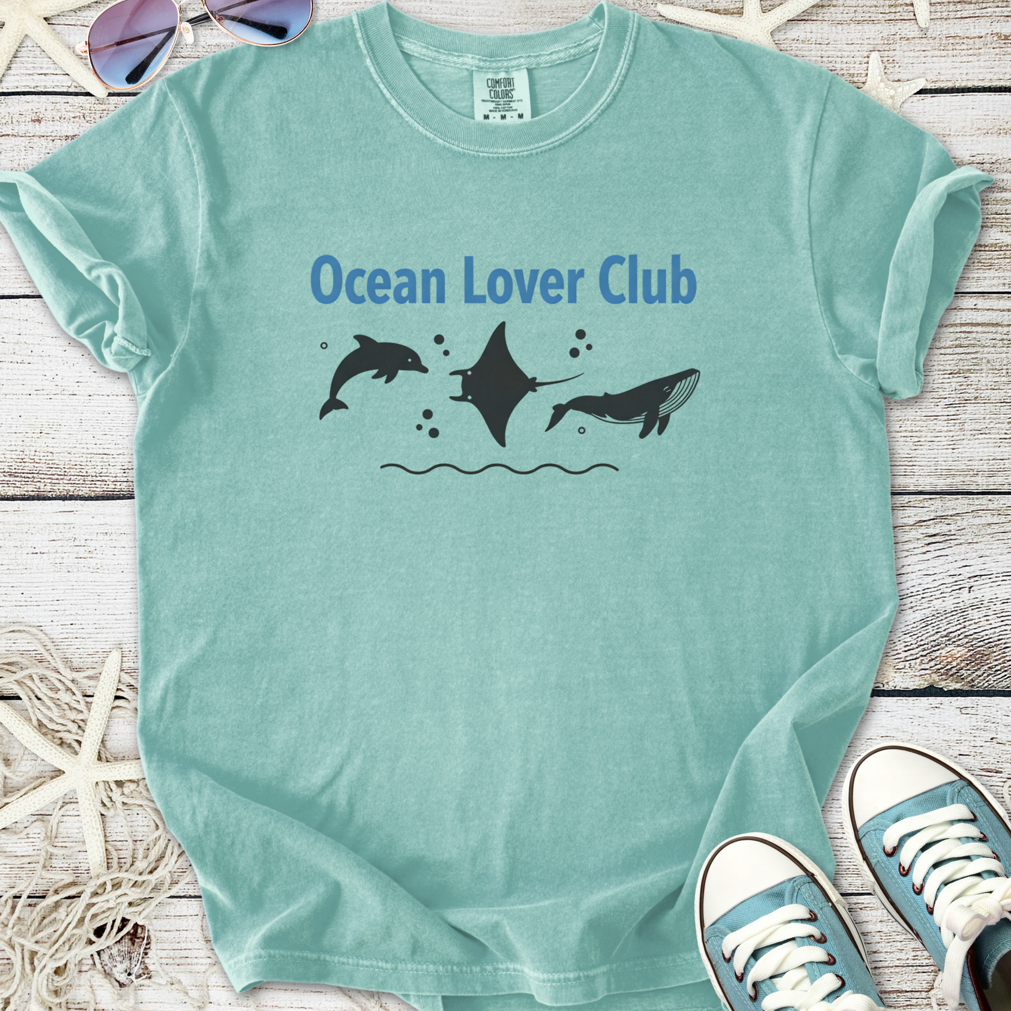 Light teal t-shirt with 'Ocean Lover Club' design featuring dolphins, a manta ray, and a whale.