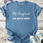 Blue graphic t-shirt with the phrase 'life happens, THE BEACH HELPS' in white lettering