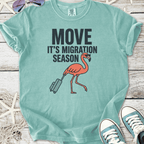 Light teal t-shirt featuring a flamingo with a suitcase and text 'Move It's Migration Season'.