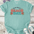 A teal cotton t-shirt with a fun 'Bad Day? BEACH DAY' graphic and floral design, perfect for summer.