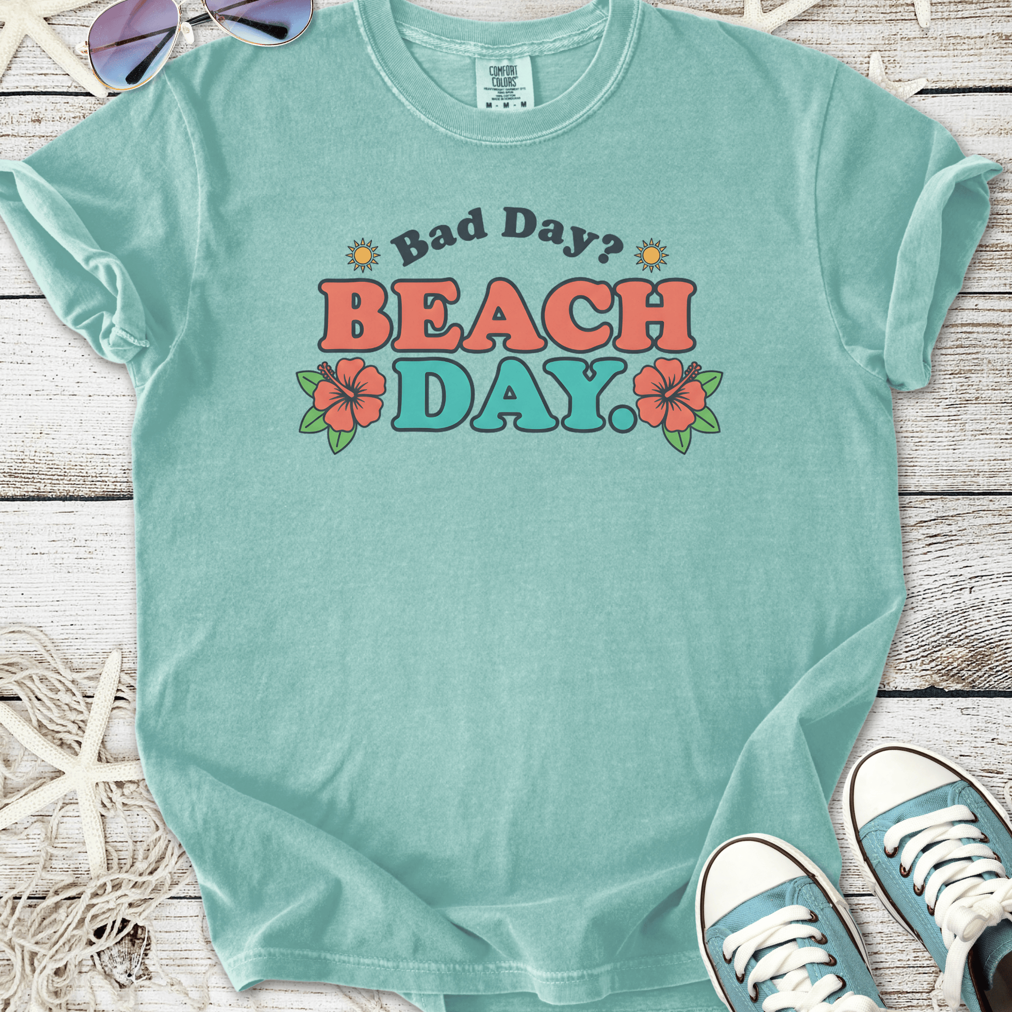 A teal cotton t-shirt with a fun 'Bad Day? BEACH DAY' graphic and floral design, perfect for summer.