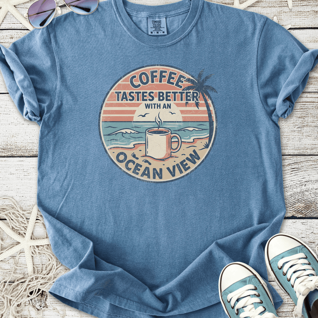 Blue t-shirt with 'Coffee Tastes Better with an Ocean View' graphic, perfect for casual beach vibes.