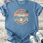 Blue t-shirt with 'Coffee Tastes Better with an Ocean View' graphic, perfect for casual beach vibes.