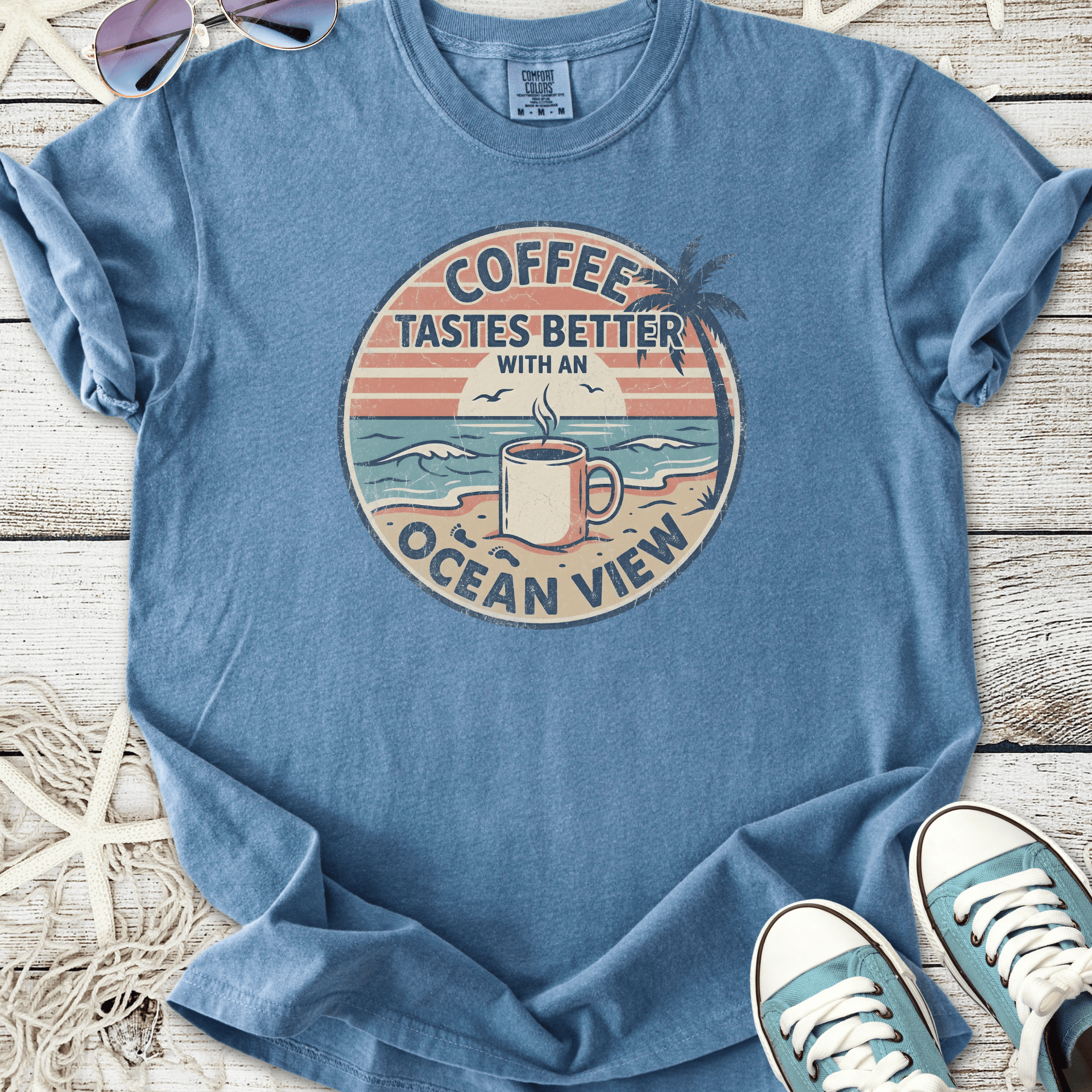 Blue t-shirt with 'Coffee Tastes Better with an Ocean View' graphic, perfect for casual beach vibes.