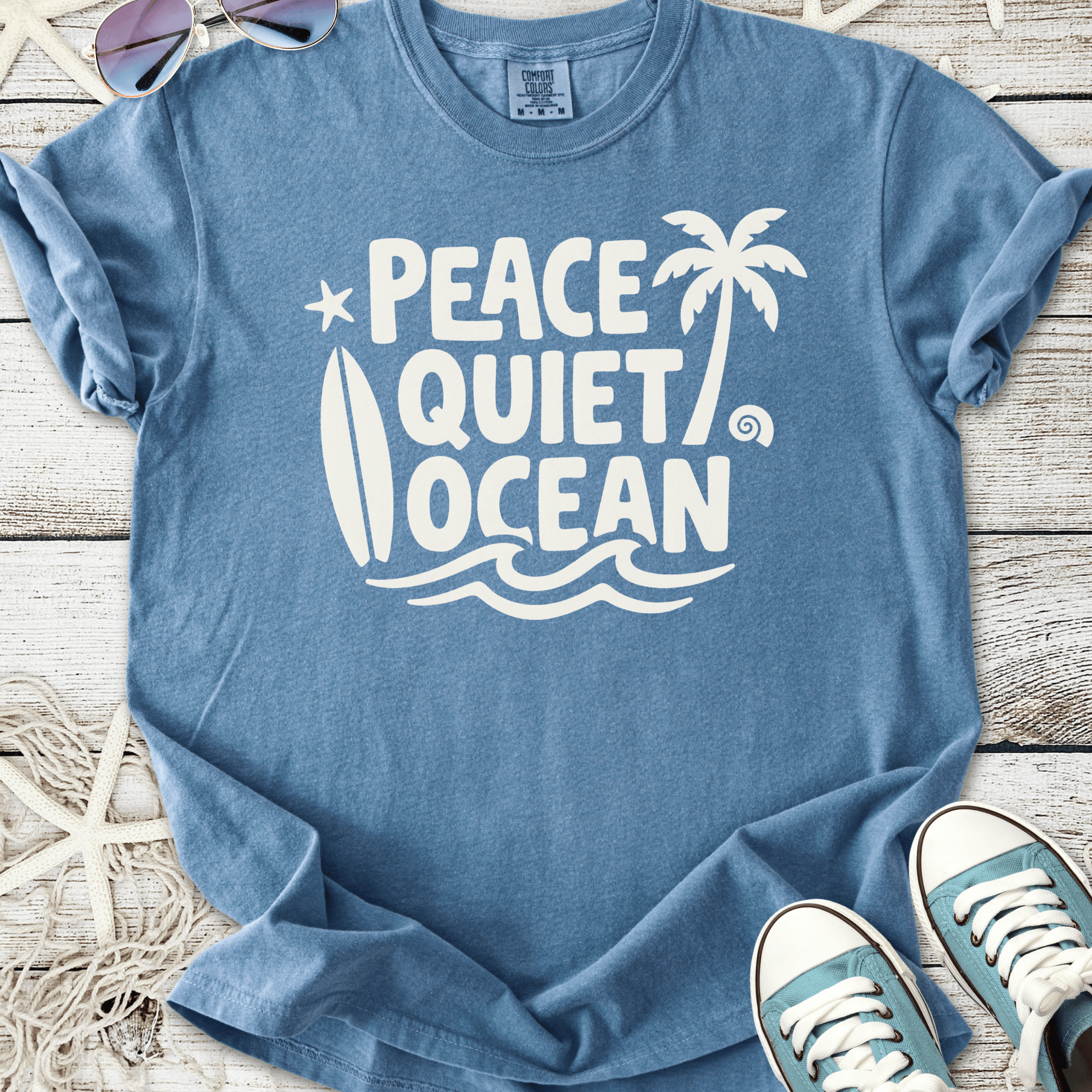 Blue graphic tee featuring 'Peace Quiet Ocean' design with surfboard and palm tree motifs.
