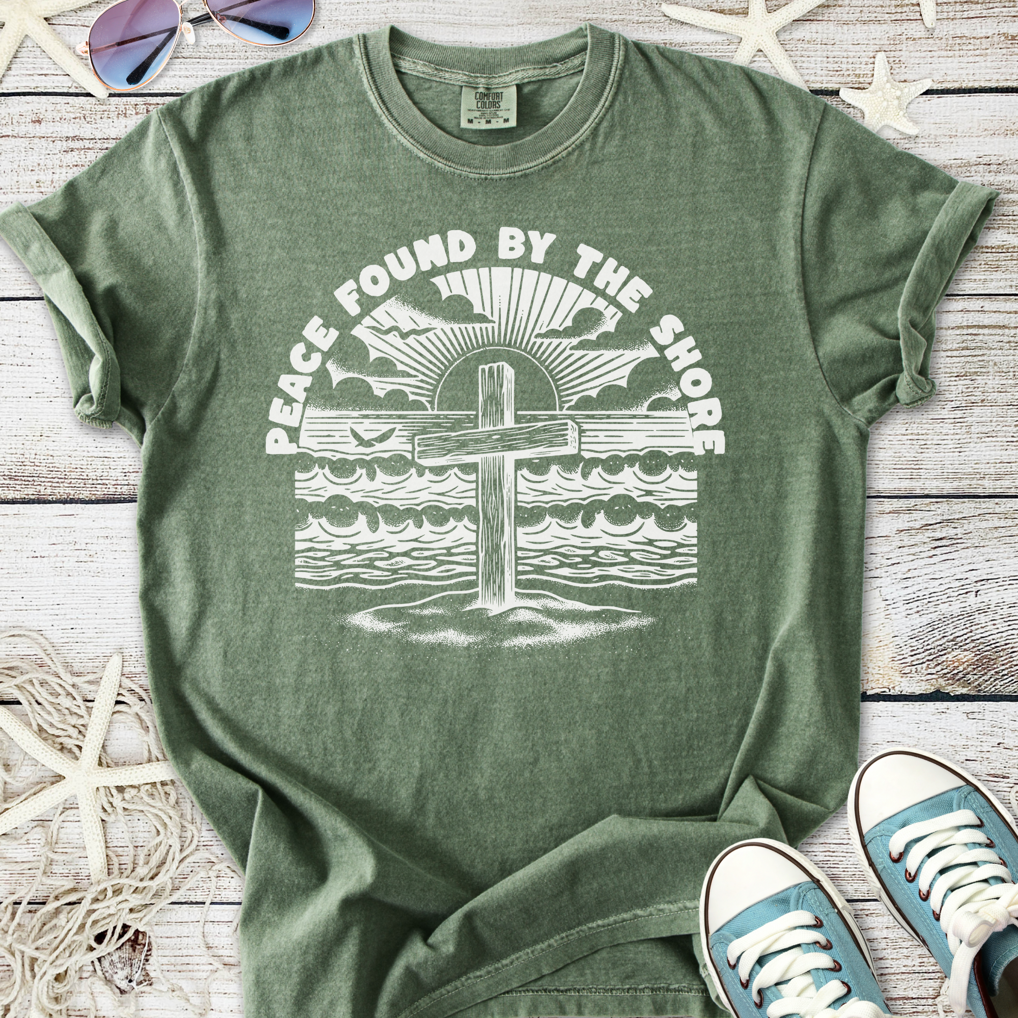 Green unisex t-shirt featuring a beach cross design with the text 'Peace Found By The Shore'.