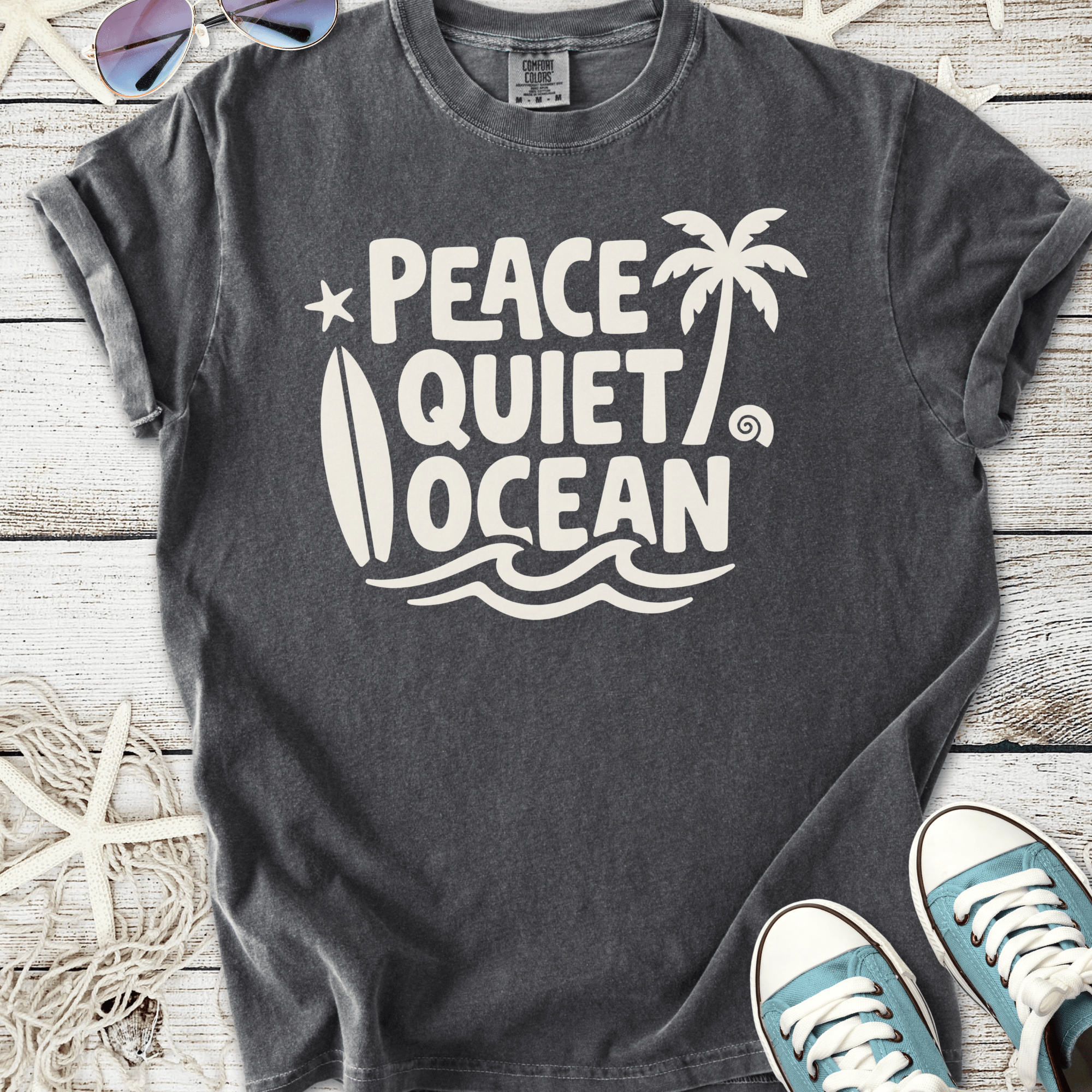 Gray graphic t-shirt featuring 'Peace Quiet Ocean' design with palm trees and surfboard, perfect for beach lovers.