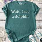 Teal graphic t-shirt with ‘Wait, I see a dolphin’ text, perfect for casual beachwear.