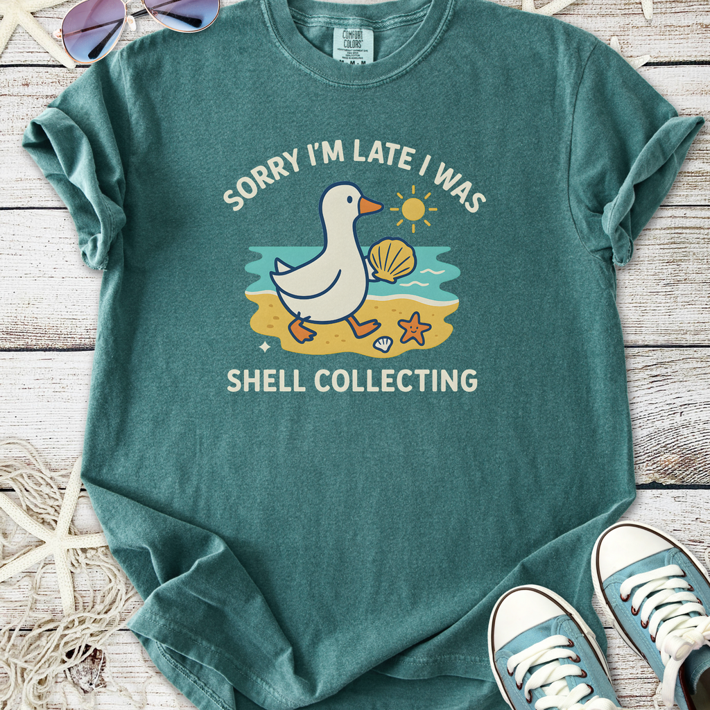 Teal graphic t-shirt with duck and shell collecting illustration, perfect for casual beach outings.