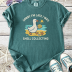 Teal graphic t-shirt with duck and shell collecting illustration, perfect for casual beach outings.