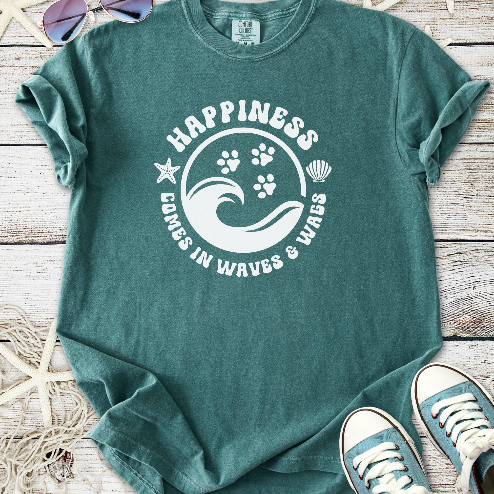 Teal graphic t-shirt with 'Happiness Comes in Waves & Wags' design and paw prints, ideal for beach lovers.